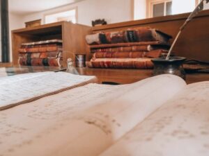 Open book, old books, and a quill arranged on a desk, representing reading, learning, and imagination